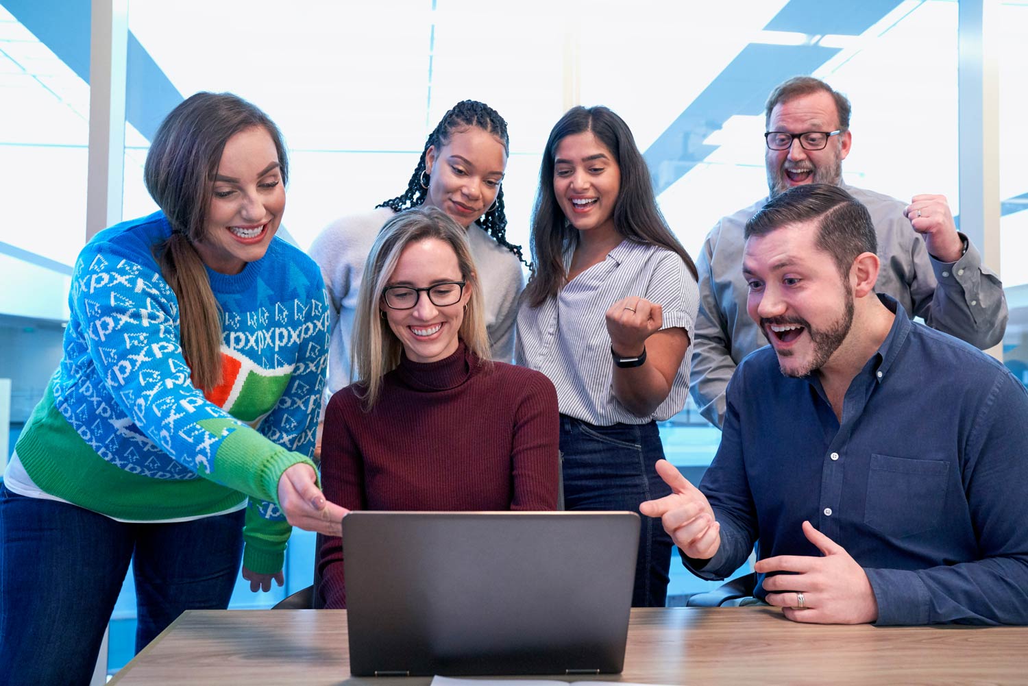 Happy people gathered around a laptop pointing at the screen with excitement